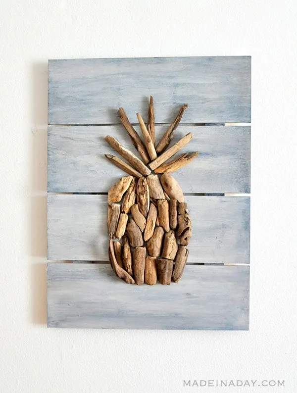 Pieces of driftwood arranged into a pineapple shape mounted on a white washed wood background.