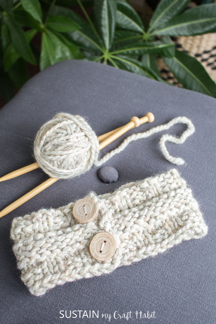 Knitted headband next to yarn and knitting needles.