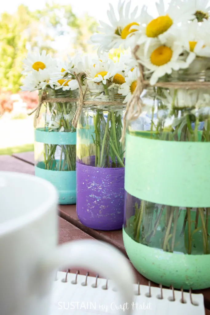 Close up of mason jar summer table centerpieces with daisies.
