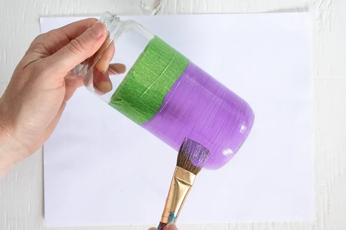 Painting the bottom of a mason jar with purple paint.