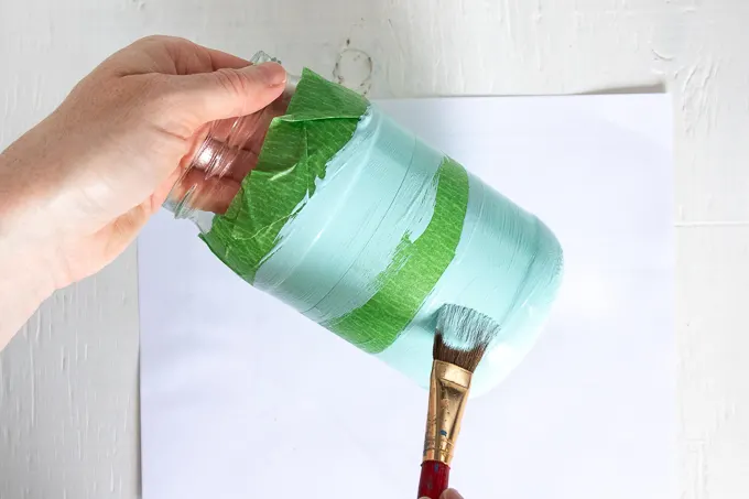 Painting the middle and bottom of a mason jar with coastal blue paint.