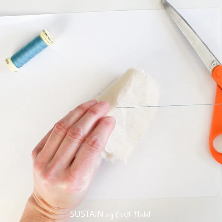 Using a needle to pull thread through a canvas fabric square.