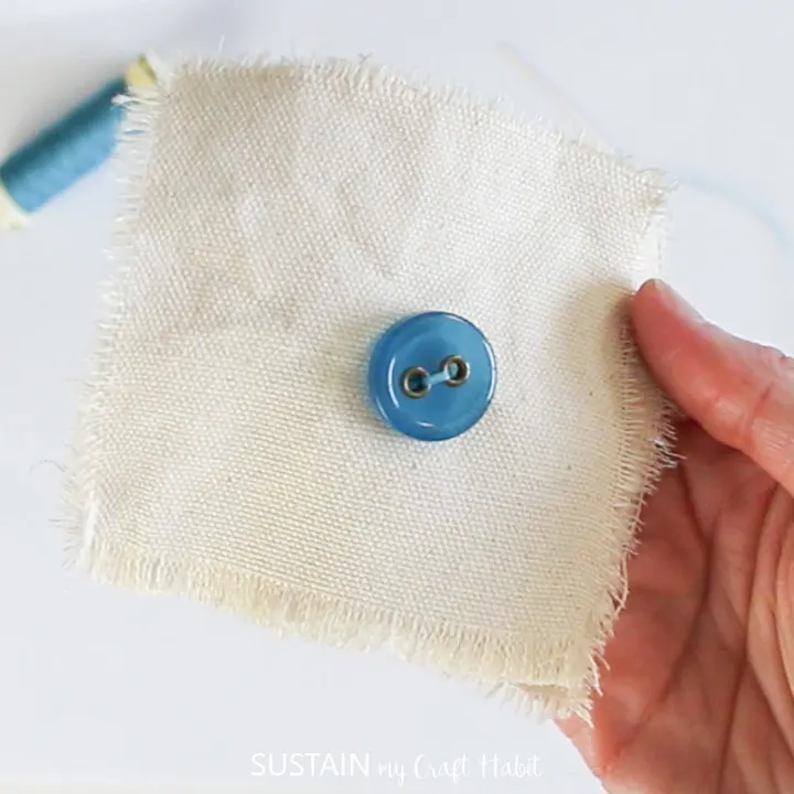 A blue button sewn onto canvas fabric.