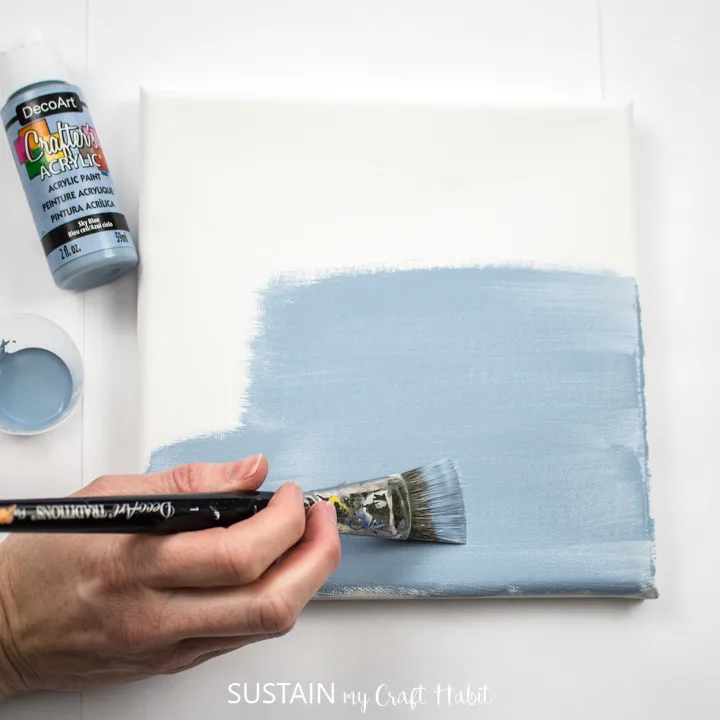 Painting a canvas with blue paint.