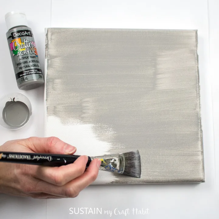 Painting a canvas with grey paint.