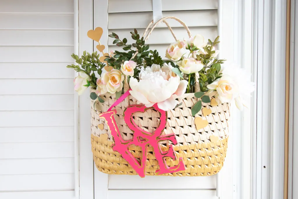 Upcycled straw purse Valentine decor that has been painted, filled with flowers and greenery and attached love sign.