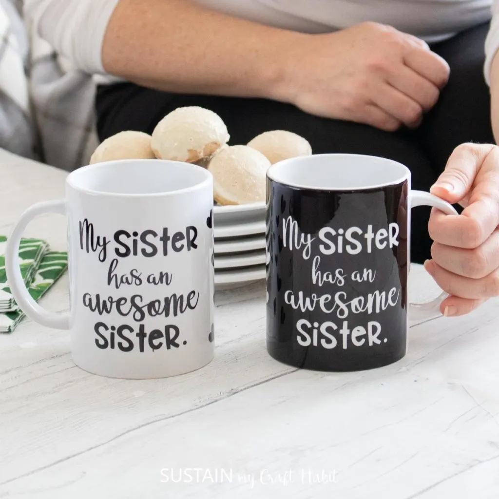 Matching black and white mugs on a white would surface table. A stack of desert plates with cookies are in the background.