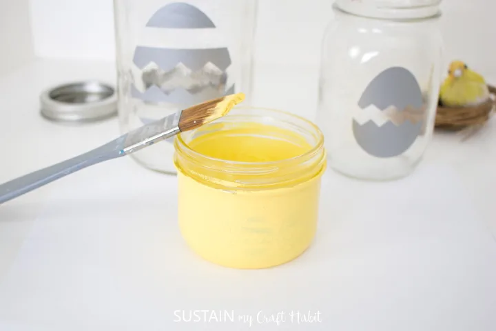 Painting a small mason jar with yellow paint.