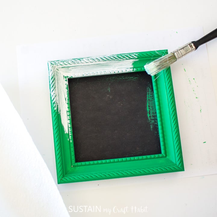 Painting white wax over a green painted picture frame.