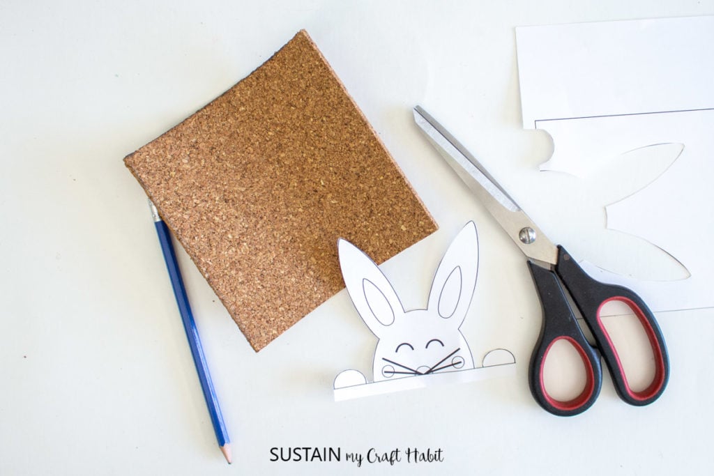 Cut out Easter bunny template next to scissors, a pencil and a cork sheet.
