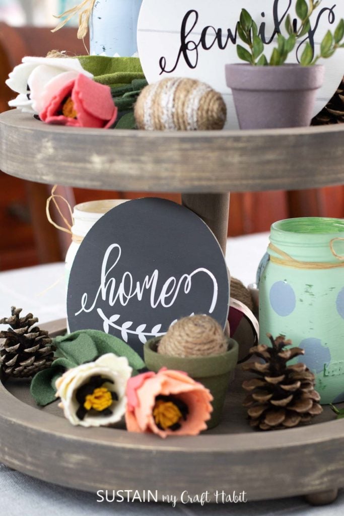 Tiered tray decorated with round wood signs, plants, flowers and Easter decor.