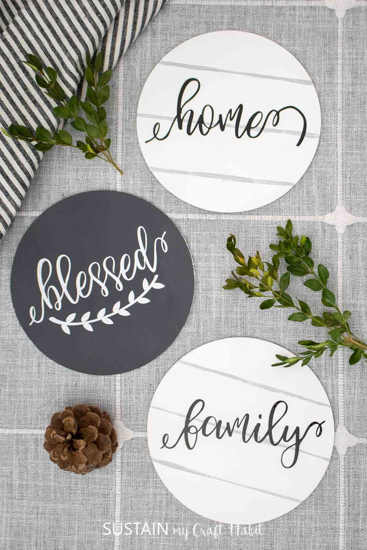 Round wood signs with vinyl lettering decorated with pine cones and greenery.