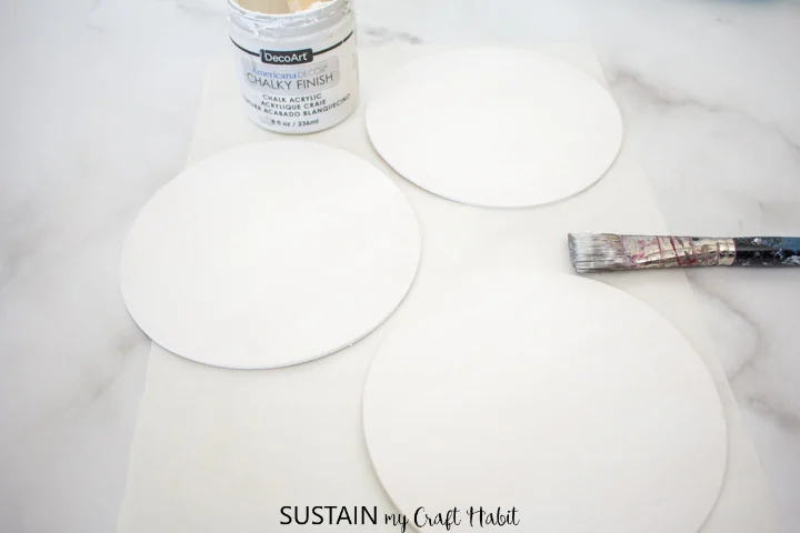Painting one side of the wood circles with white paint.