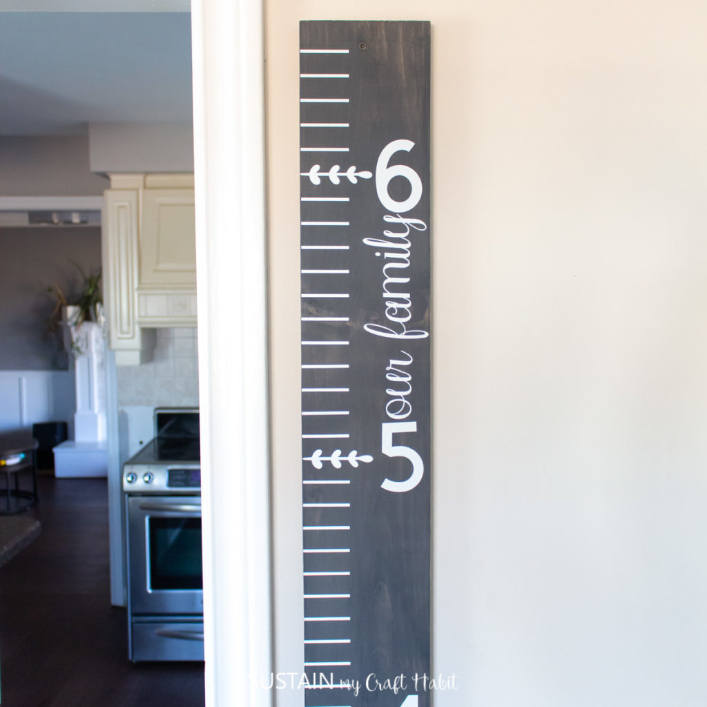 Completed gray wood DIY growth chart hanging on the wall beside the kitchen.