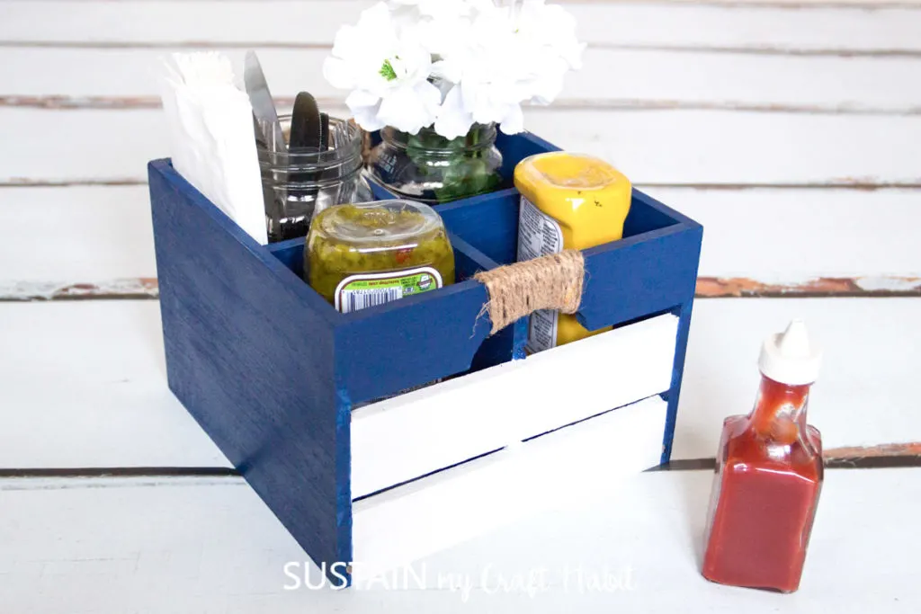 Painted BBQ caddy holding condiments, flower jar and utensils. 