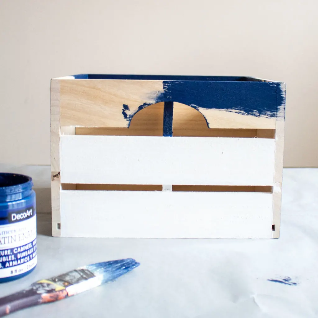 Painting the remaining sides of the wooden crate with blue paint.