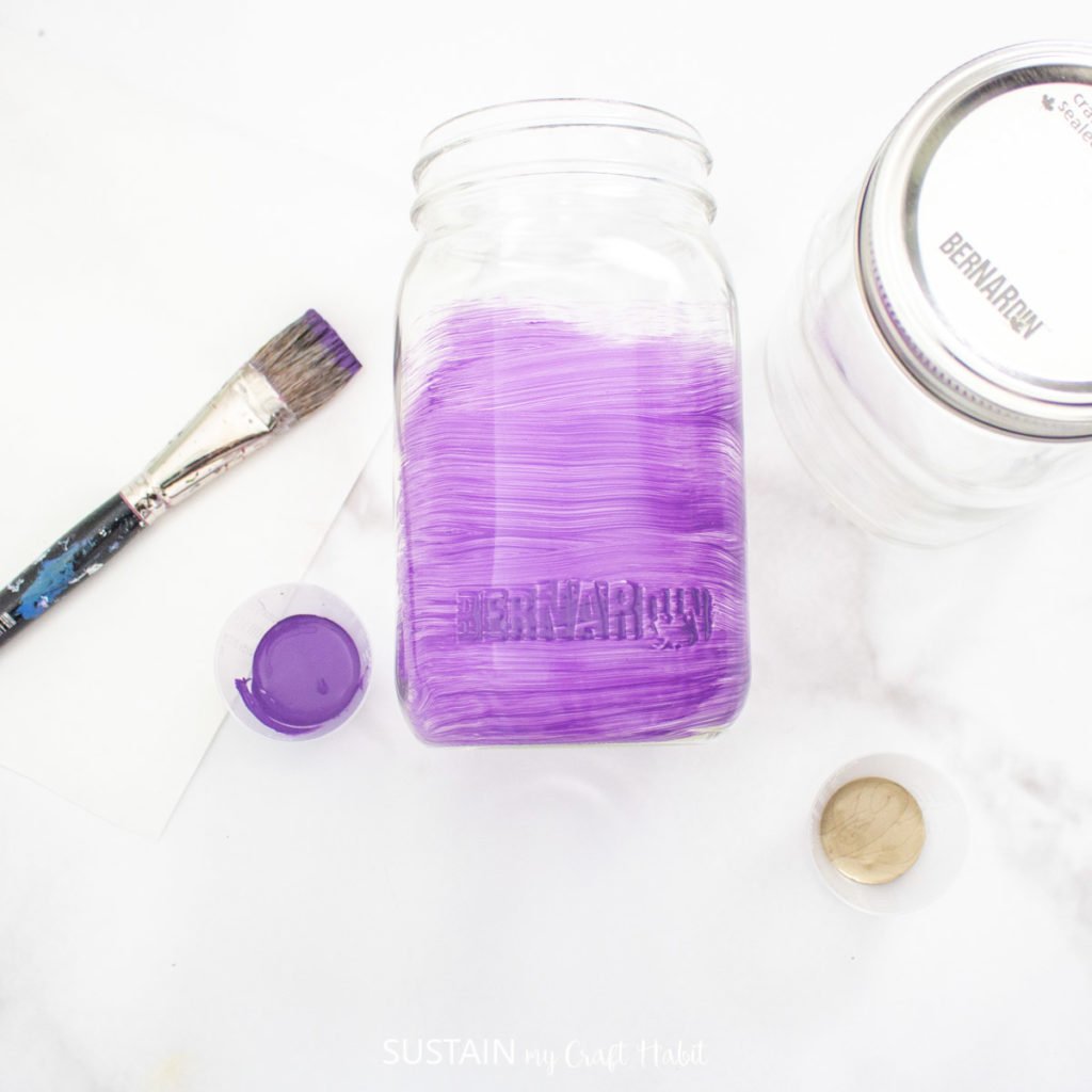 Painting a glass jar with purple paint.