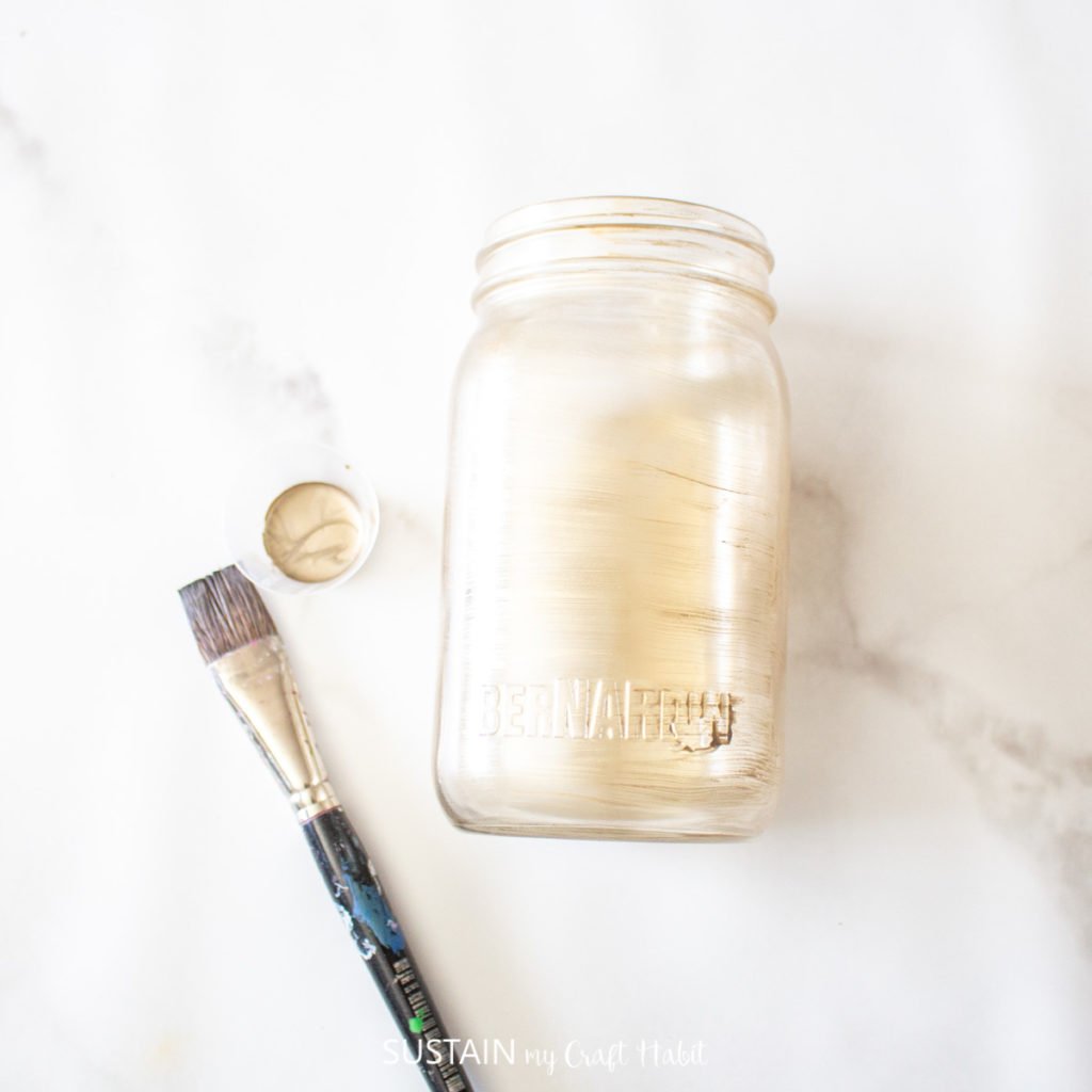 Painting a glass jar with gold paint.