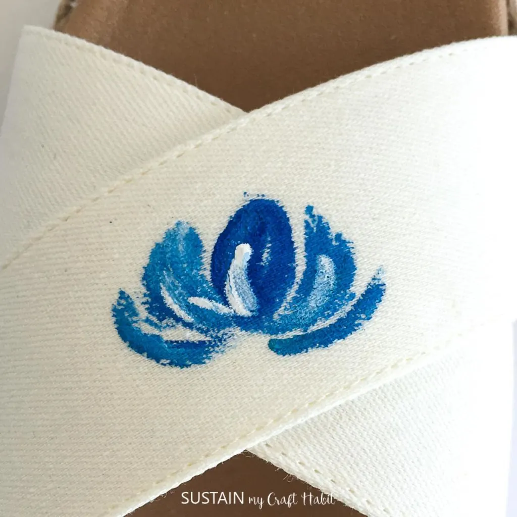 Painting more petals around the center petal on a white sandal.
