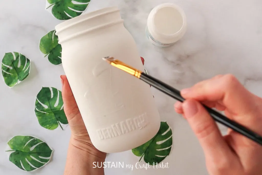 Adding a layer of Mod Podge onto the glass jar using a paint brush.
