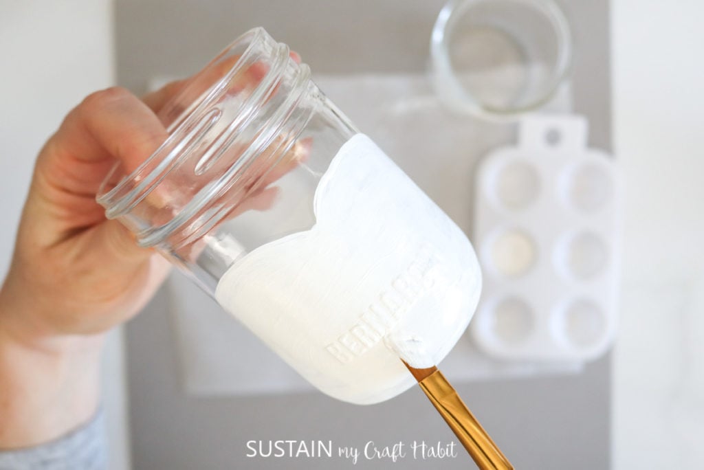 Painting a glass jar with white paint.