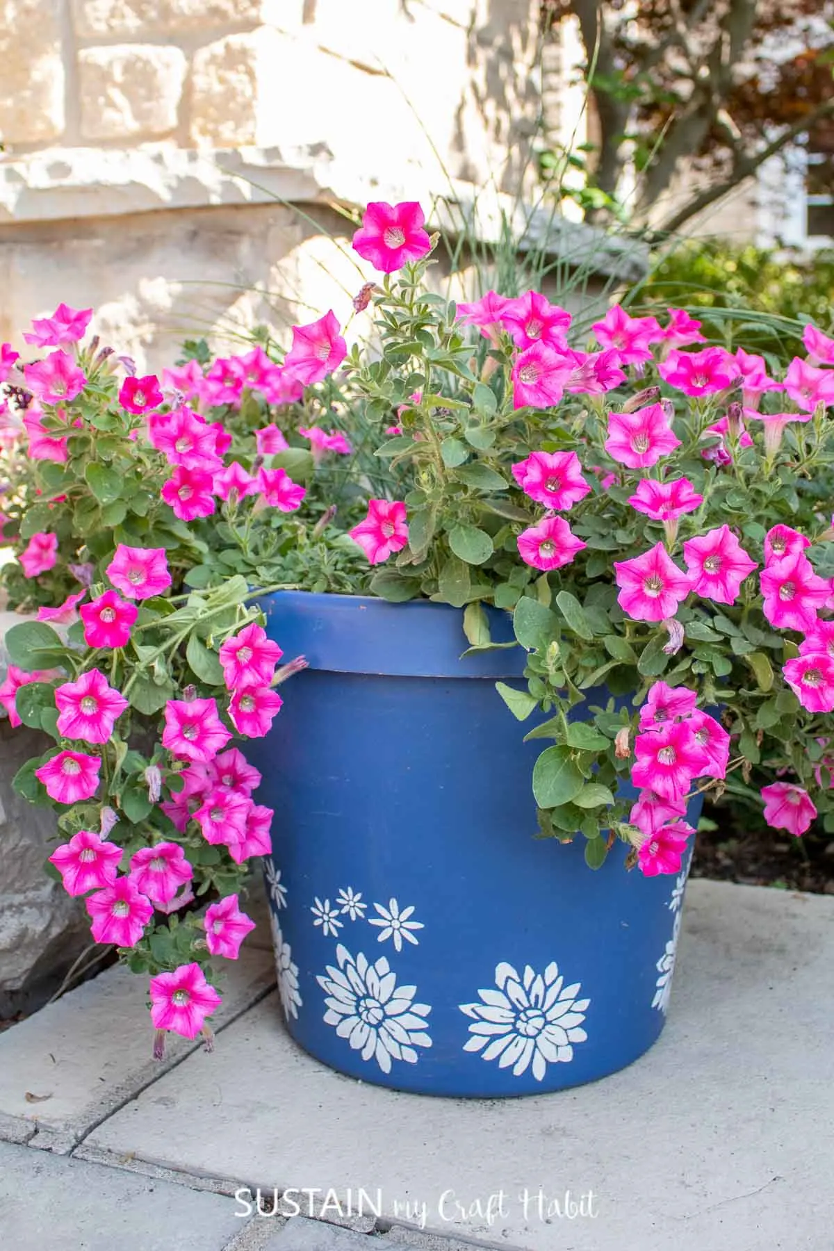 A bright blue planter with white stenciled flowers. They planter is overflowing with fresh pink flowers.