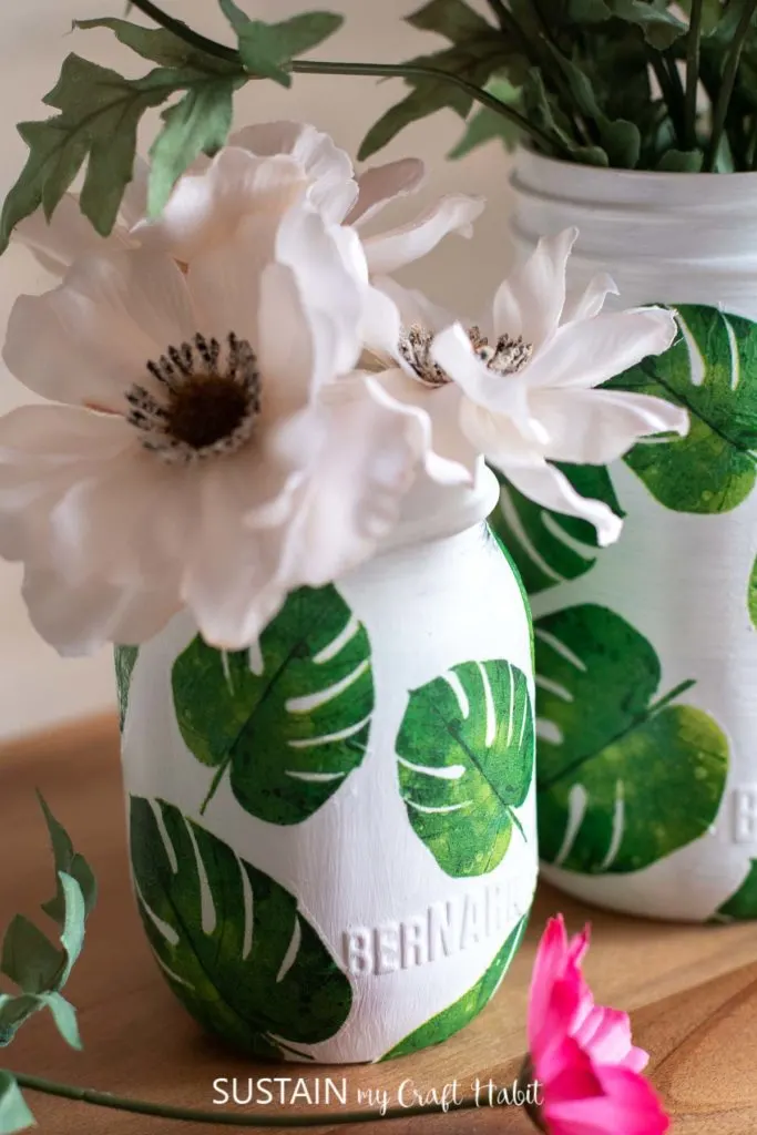 Close up of leaf napkin decoupage on glass jars filled with flowers.