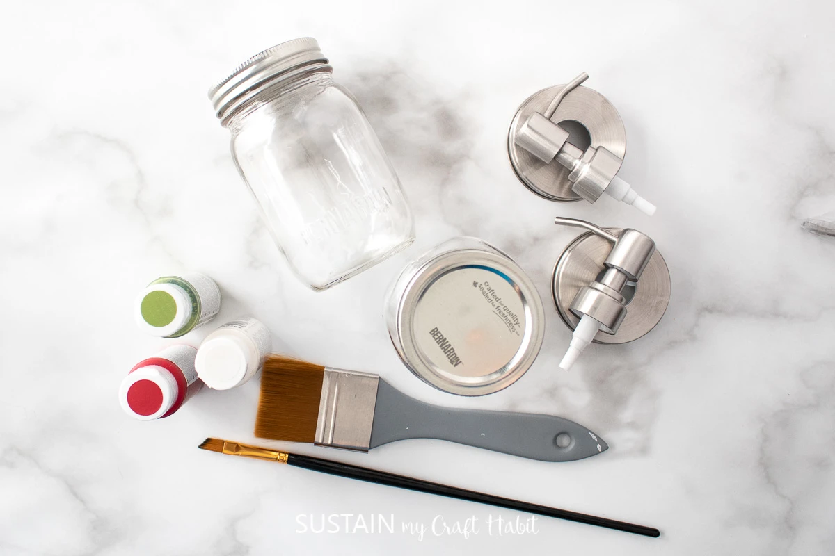 Materials needed to make a soap dispenser for Christmas including a mason jar, paint, paint brushes, soap dispensers.