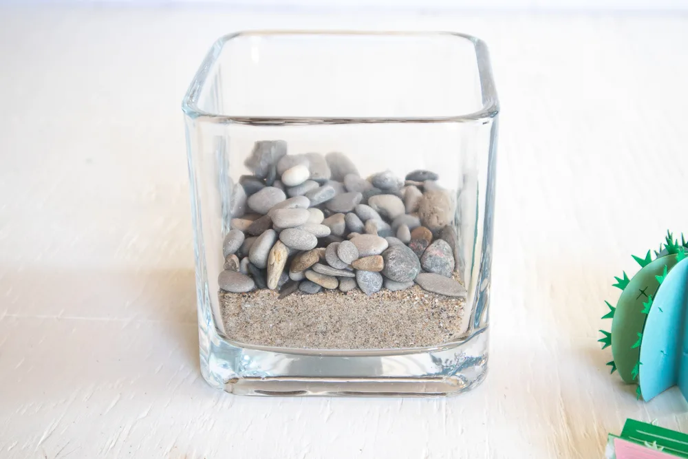 Pouring pebbles over the sand in the glass vase.