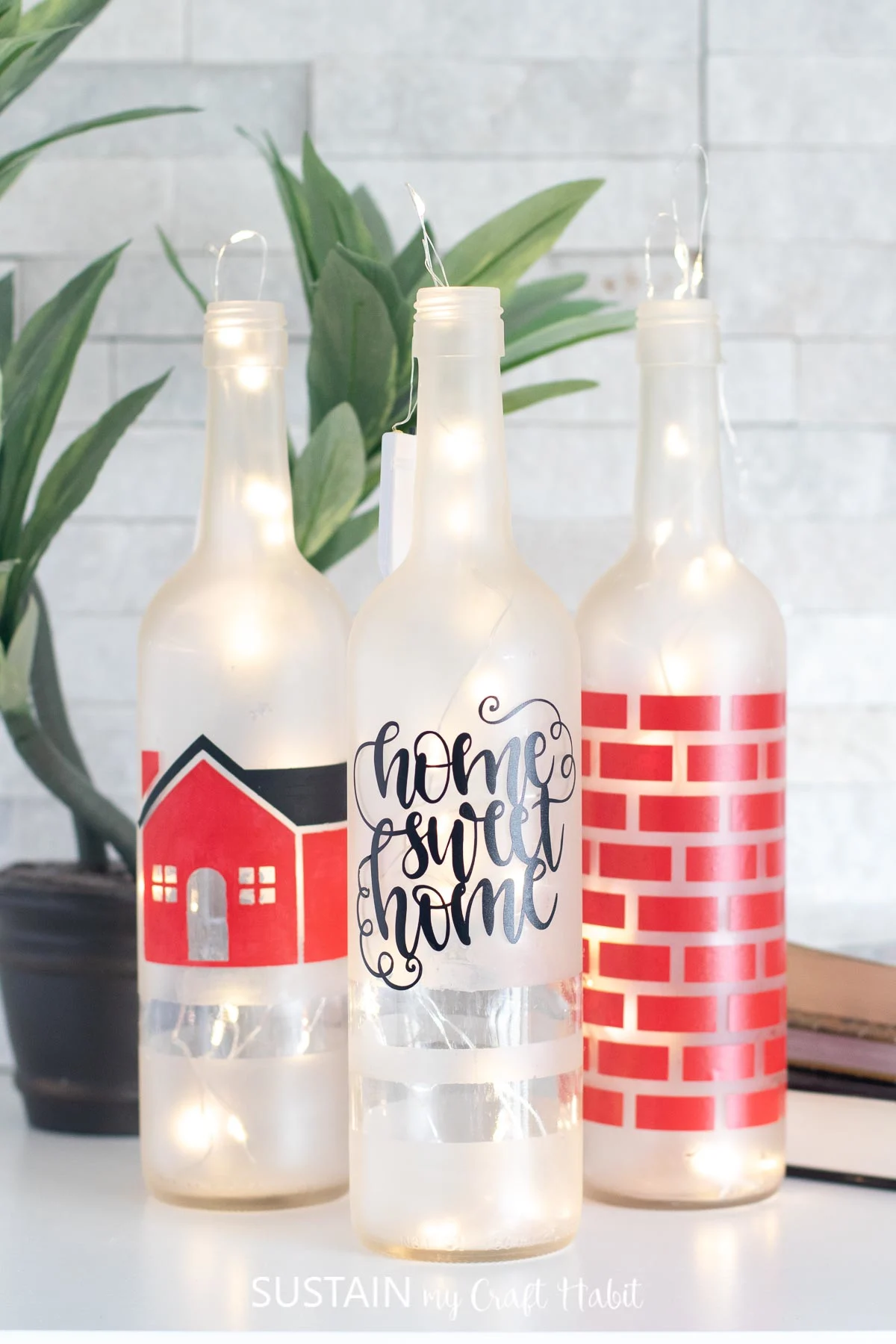 Three completed painted bottles arranged in a cluster on a white surface. Lit twinkle lights are eluminating the frosted bottles. 