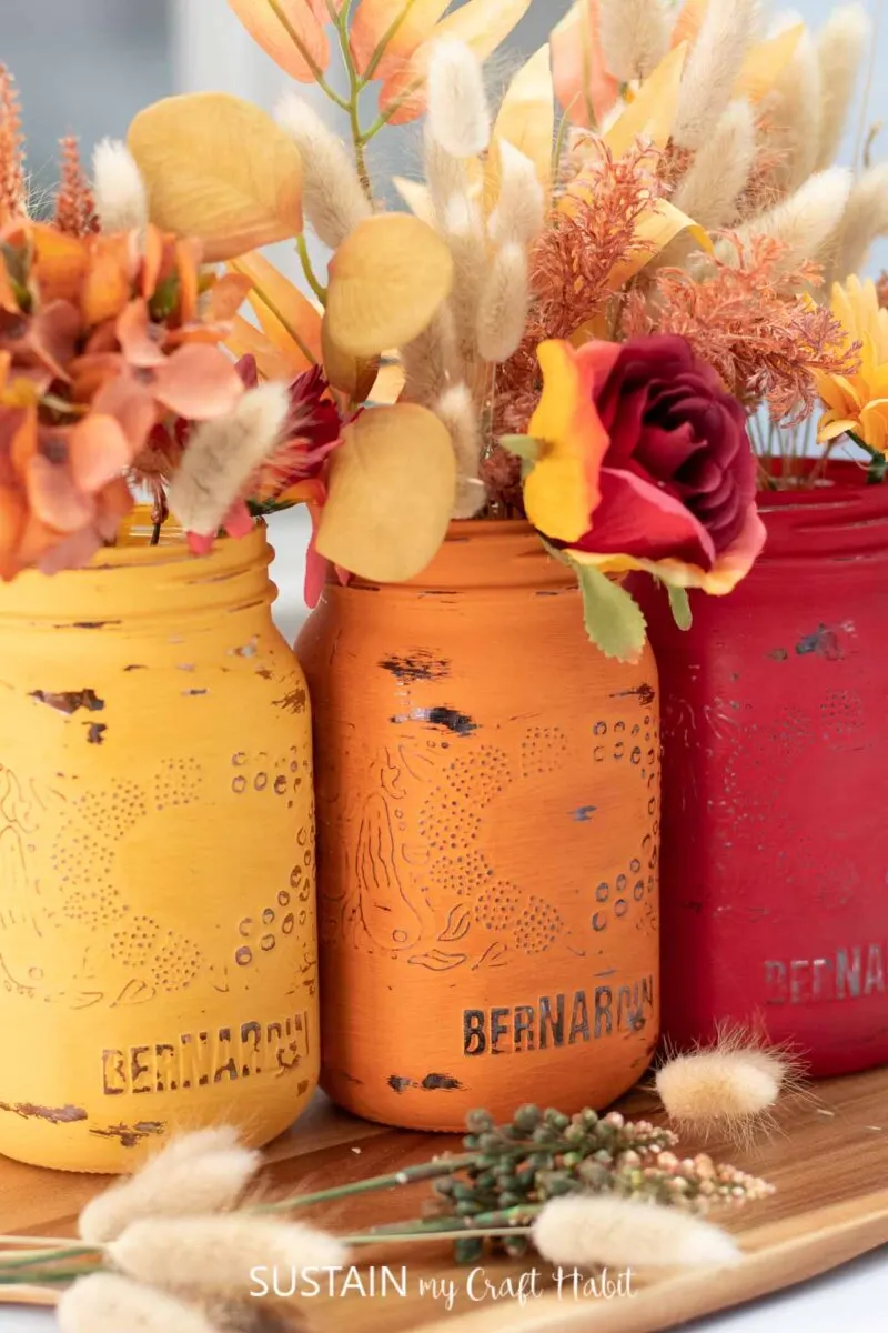Close up of painted jars for Thanksgiving filled with fall flowers and lagurus bunches.