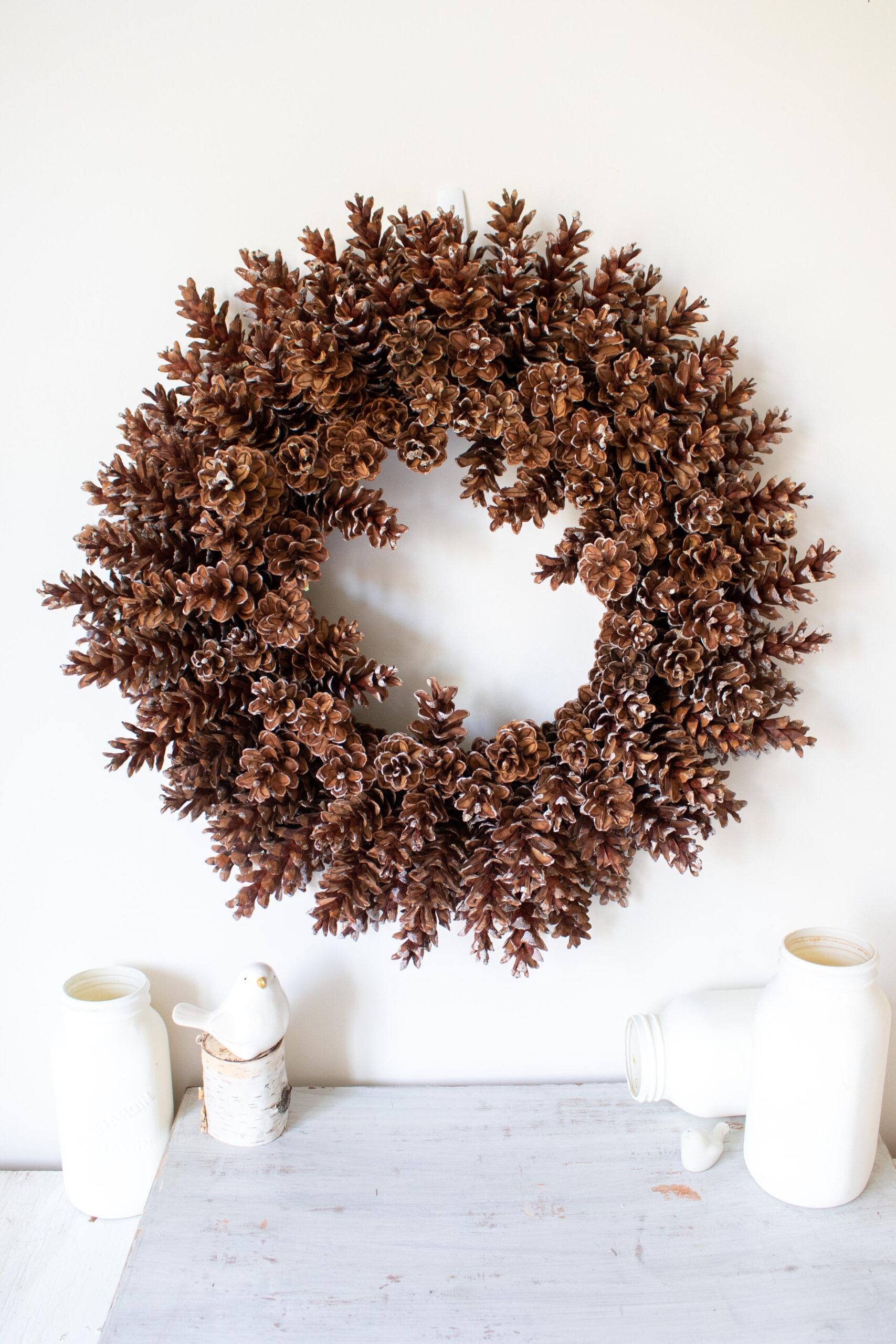 Completed pineone wreath hung on a wall with white accessories.
