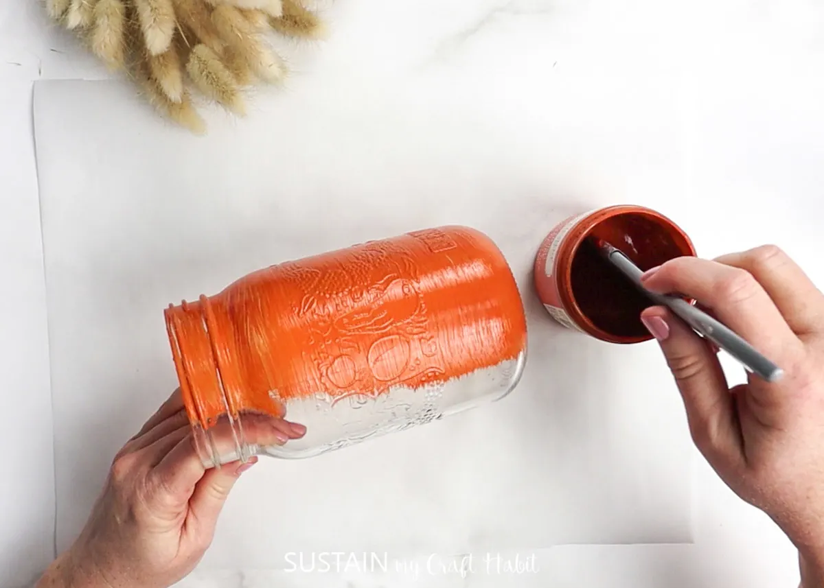 Painting a mason jar with orange paint.