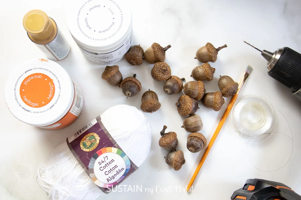 Materials needed to make an acorn garland, including acorns, paint, paint brush, drill, and string.