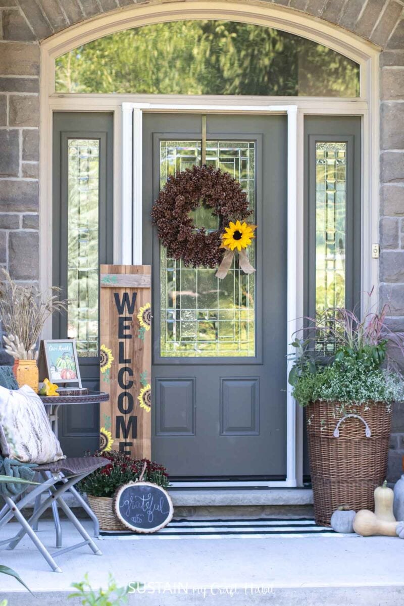 Porch decorated for fall with wooden signs, planter, wreath and accessories.