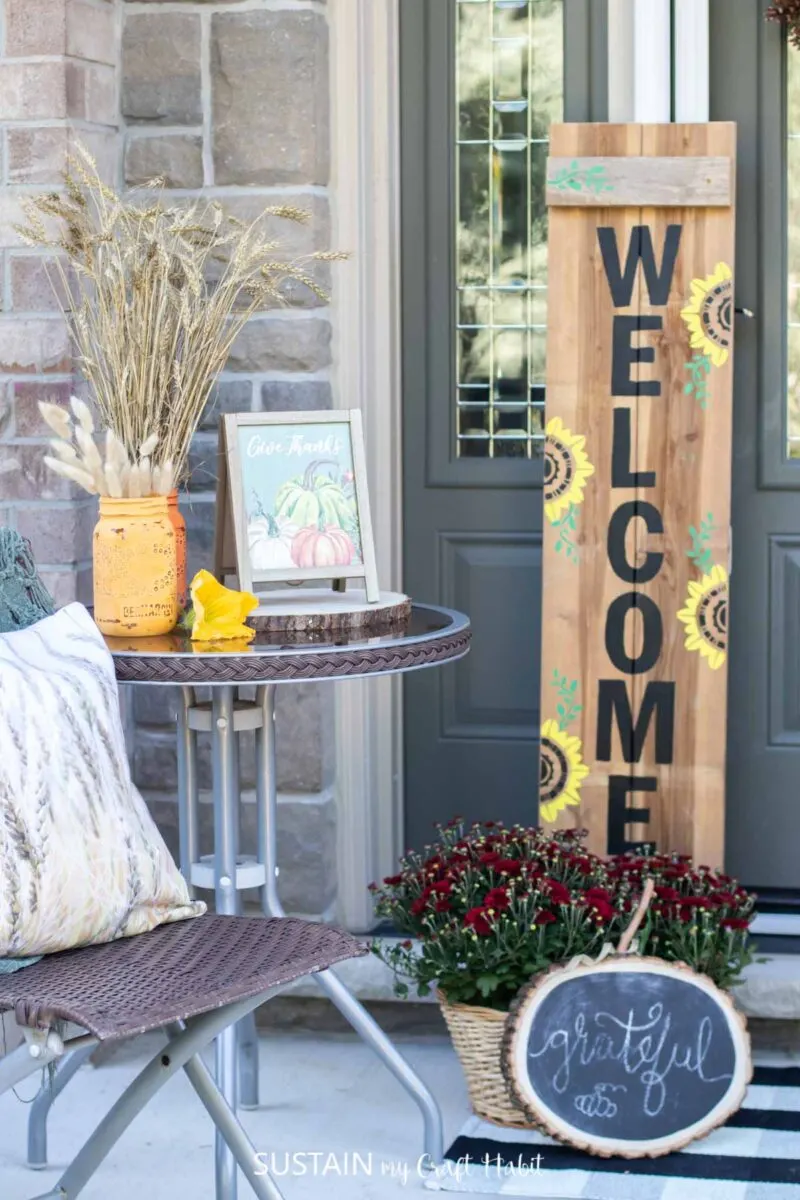 Wooden welcome sign next to a table and chairs with fall accessories.