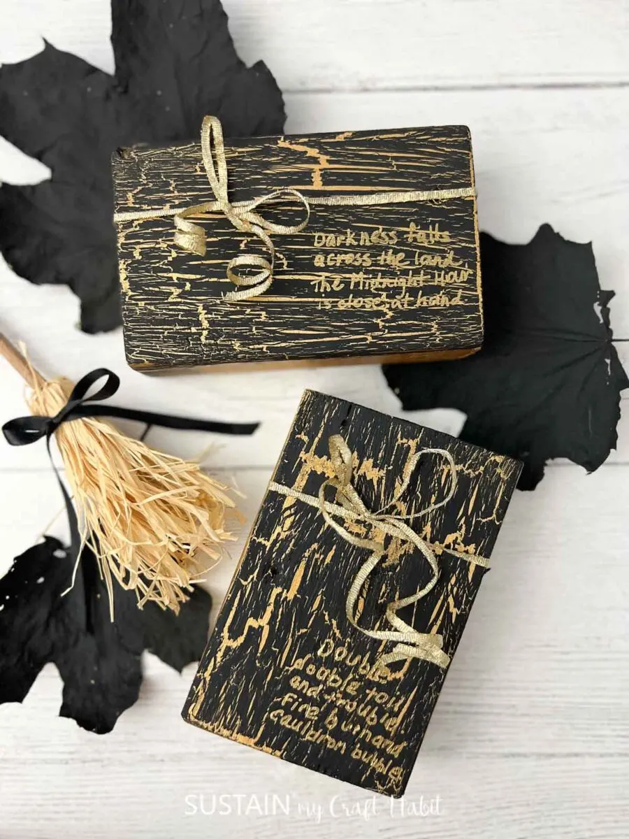 Two small wood blocks painted with a black crackle paint finish over a gold paint base. Each block has a gold phrase written on them and are surrounded by decorative elements for Halloween.