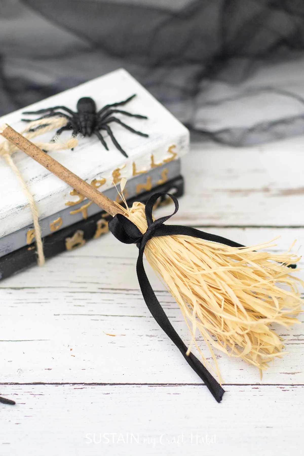 Mini witches broom leaning on stacked books with a faux spider.