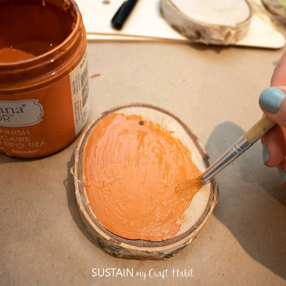 Painting a wood slice orange.