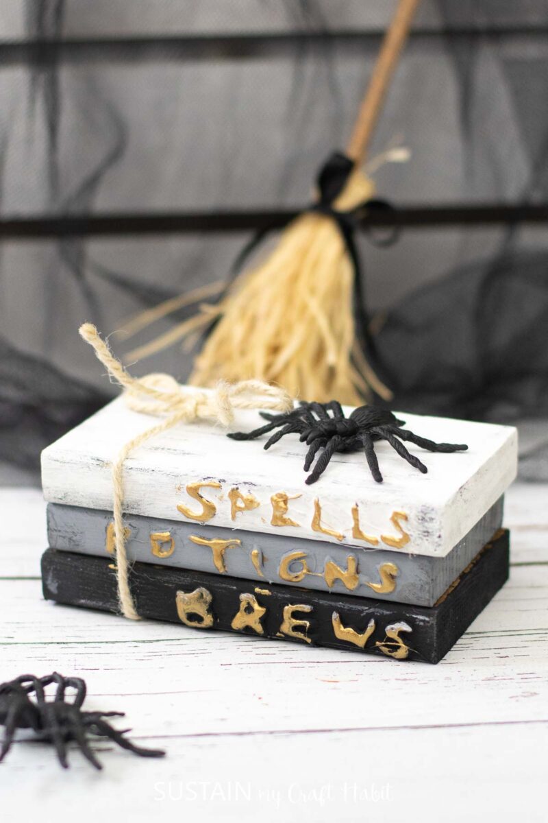 Stacked book decor with the words "spells, potions, brews" painted on the book spine for Halloween.