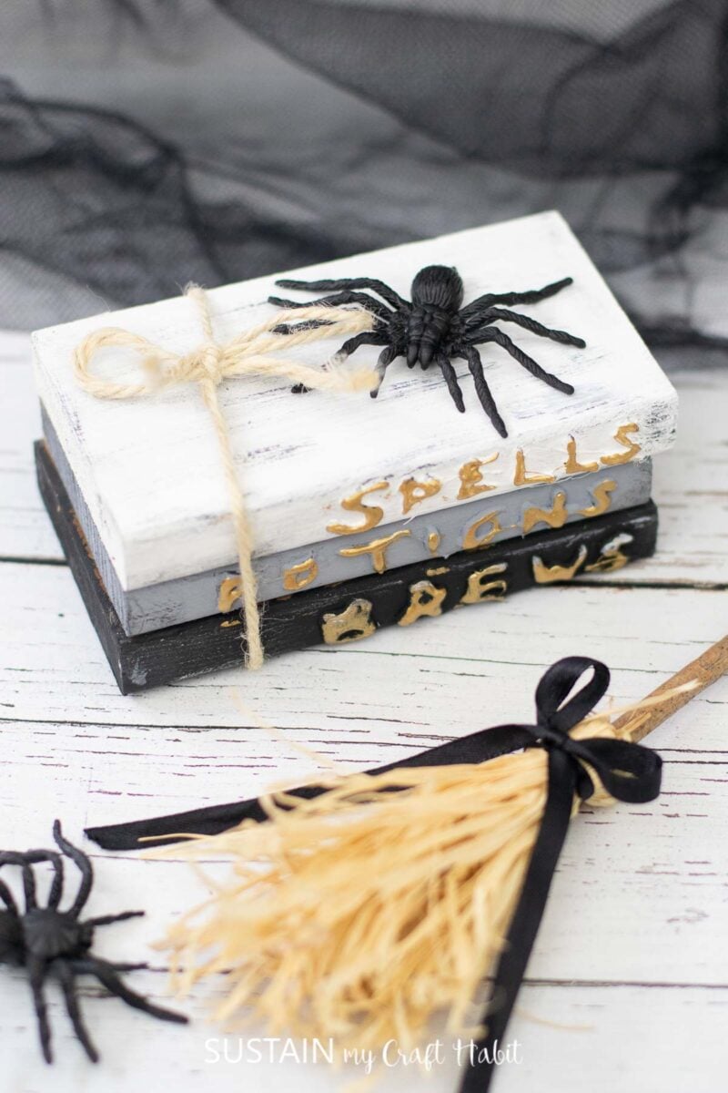Stacked book decor with the words "spells, potions, brews" painted on the front for Halloween.