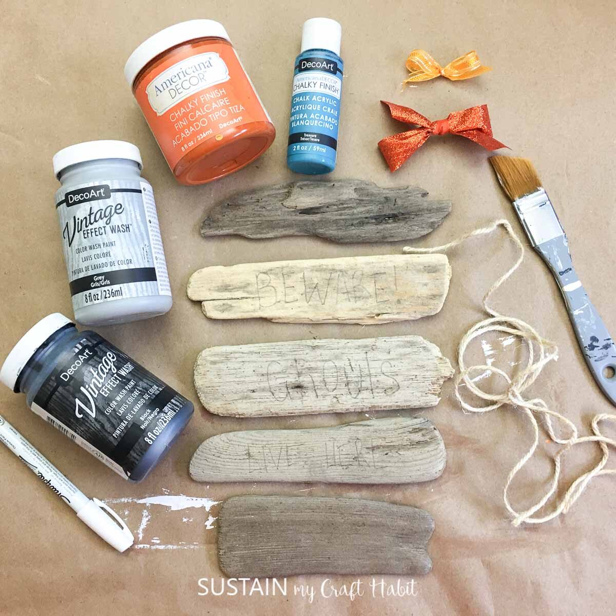 Materials needed to make a reversible driftwood wall decor for fall including driftwood, paint, paintbrush and string.
