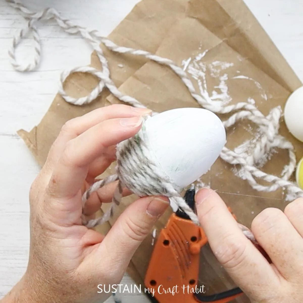 Finishing the upcycled plastic egg acorn ornament craft by gluing the yarn.