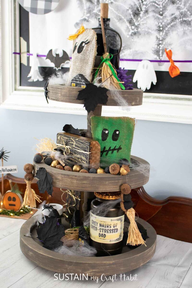 Tiered tray decor ideas for Halloween including characters, witch's brooms, stacked books, acorn garland, leaves and potion bottles.