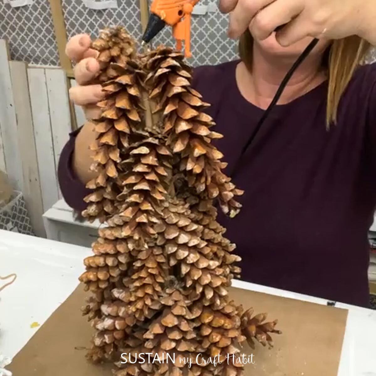 Hot gluing pine cones to the top of the cone.
