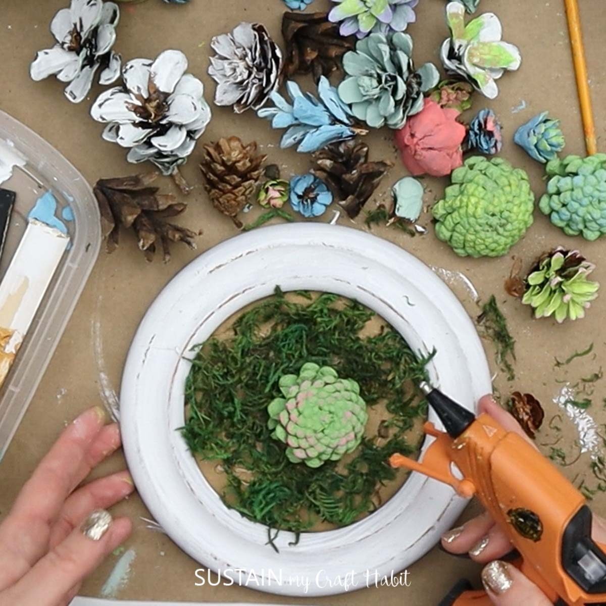 Gluing painted pine cones onto the moss.