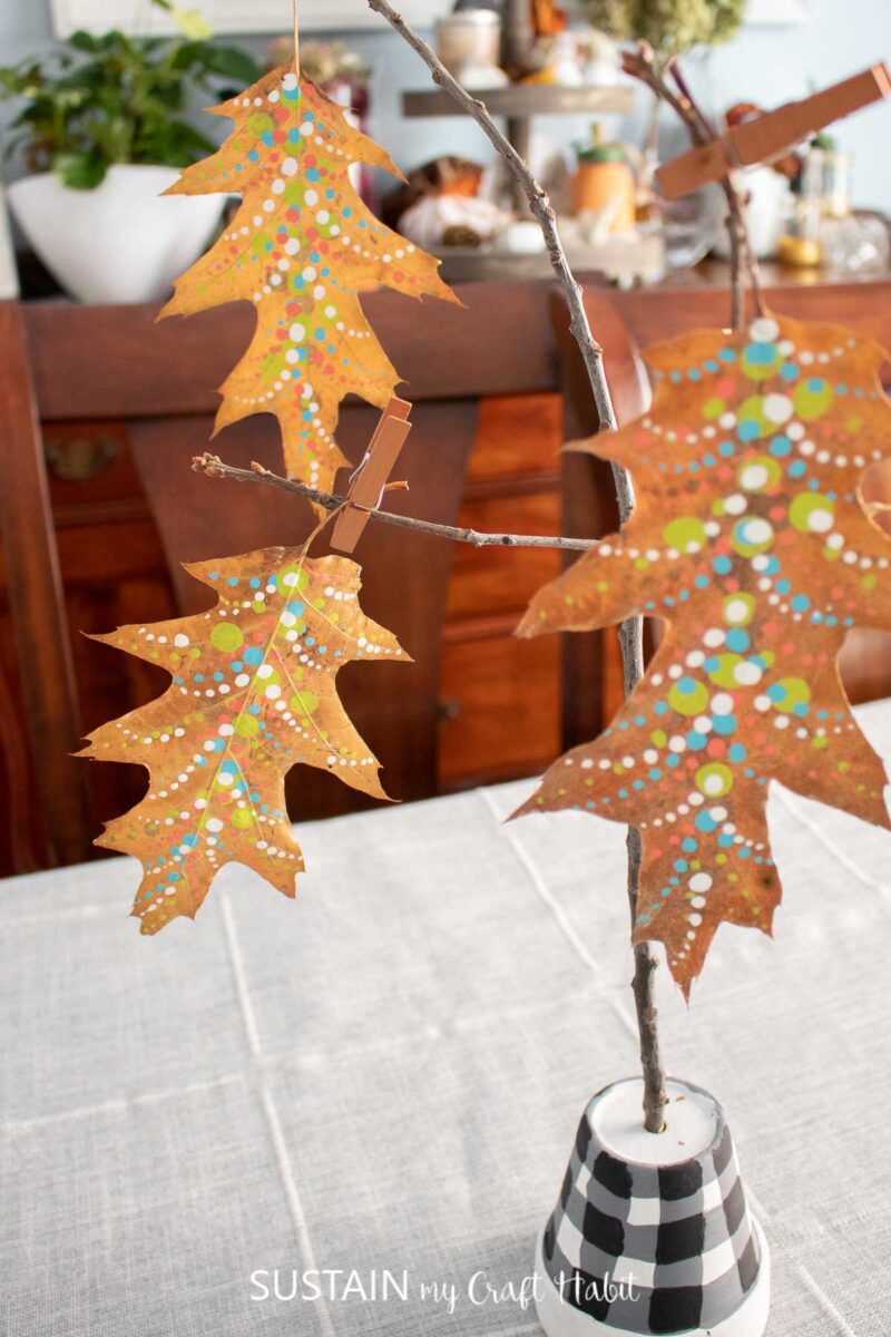 Painted pressed leaves hung on a branch with clothespins.