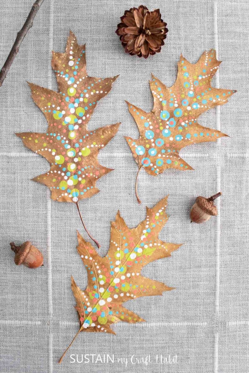 Painted pressed leaves laying on a table next to acorns.