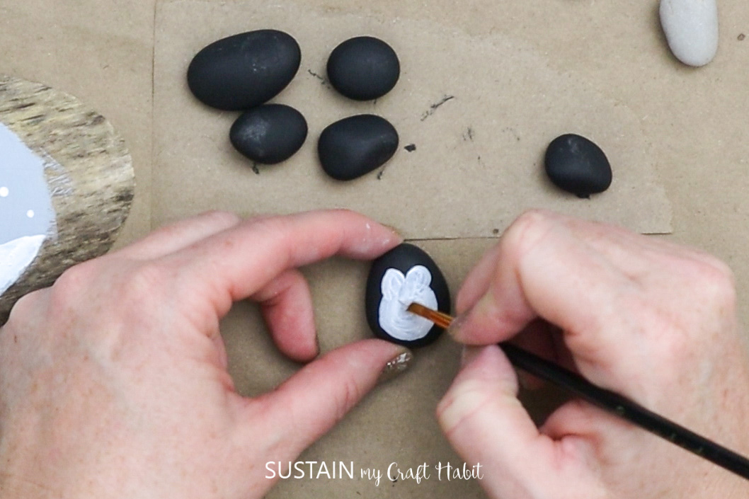 Painting penguin bodies on a pebble.