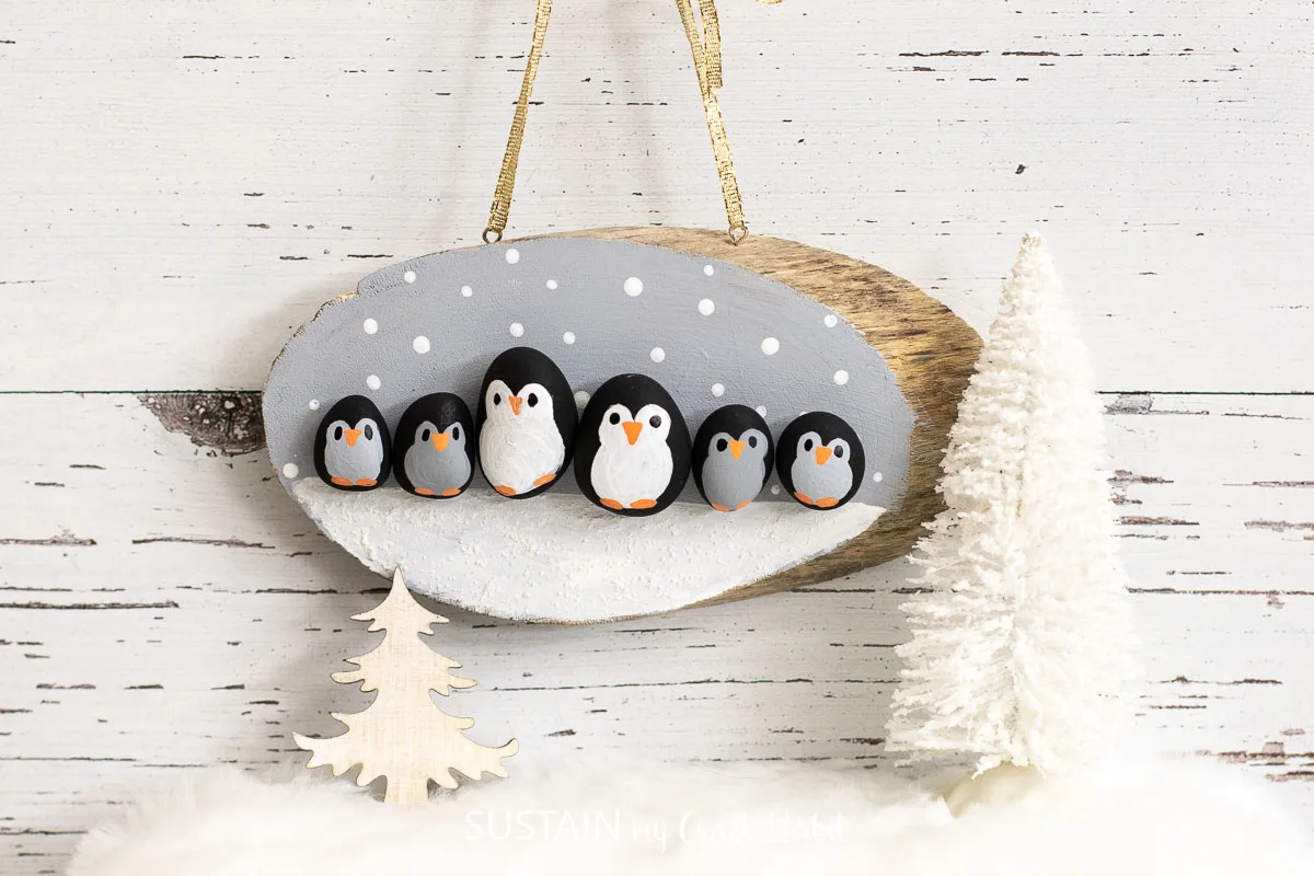 Penguin pebble art craft hanging from a wall.